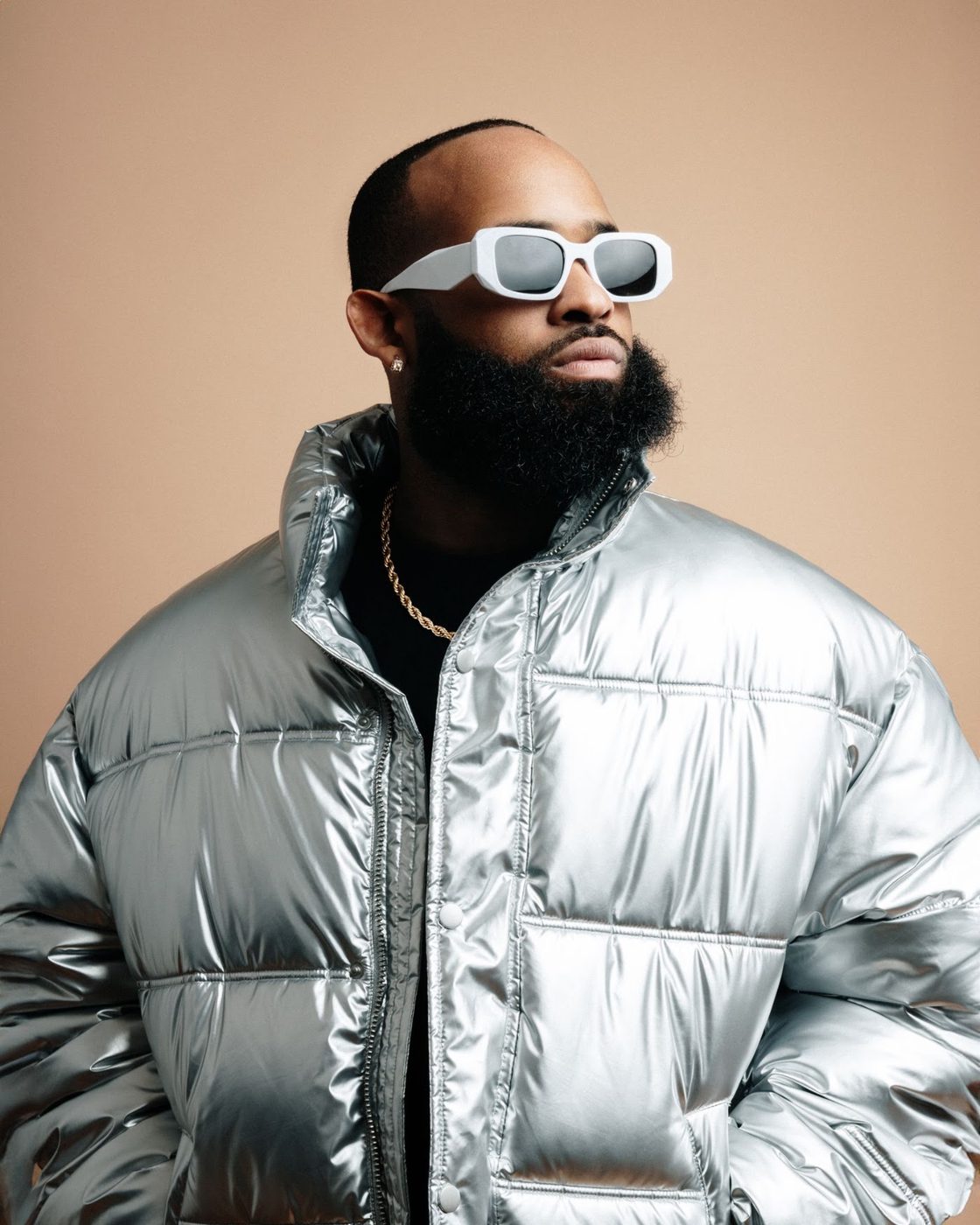Trevor Queen in a silver puffer jacket against a warm beige backdrop