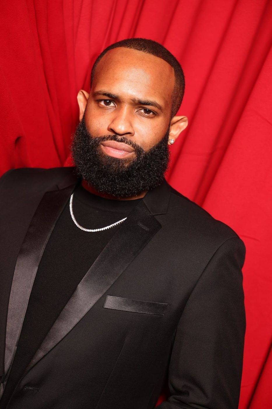 Trevor Queen in a black tuxedo against a red backdrop