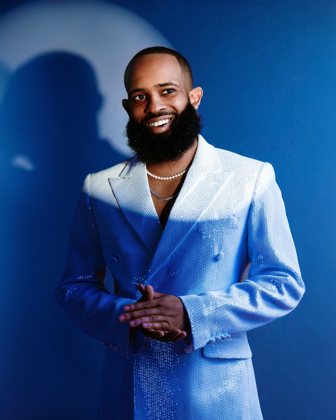 Trevor Queen smiling, hands clasped, in an ice-blue suit