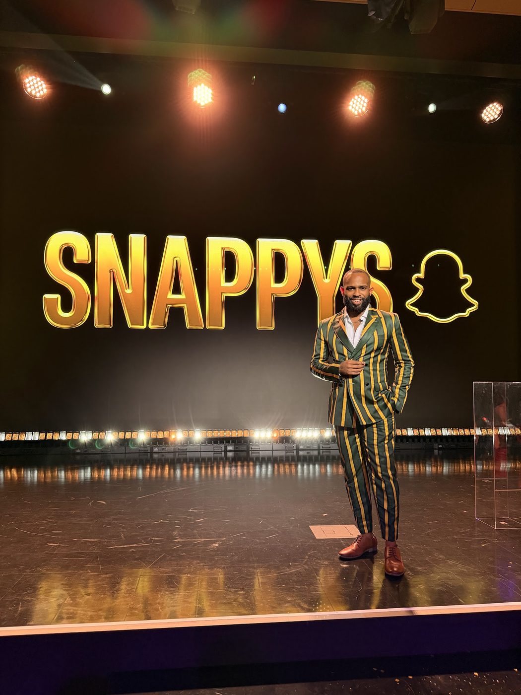 Trevor Queen speaking on stage under theatre lighting at the Snappys