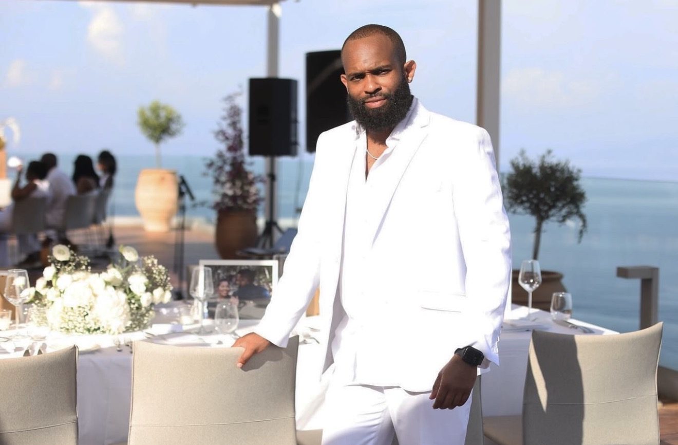 Trevor Queen in a white suit hosting an oceanside event